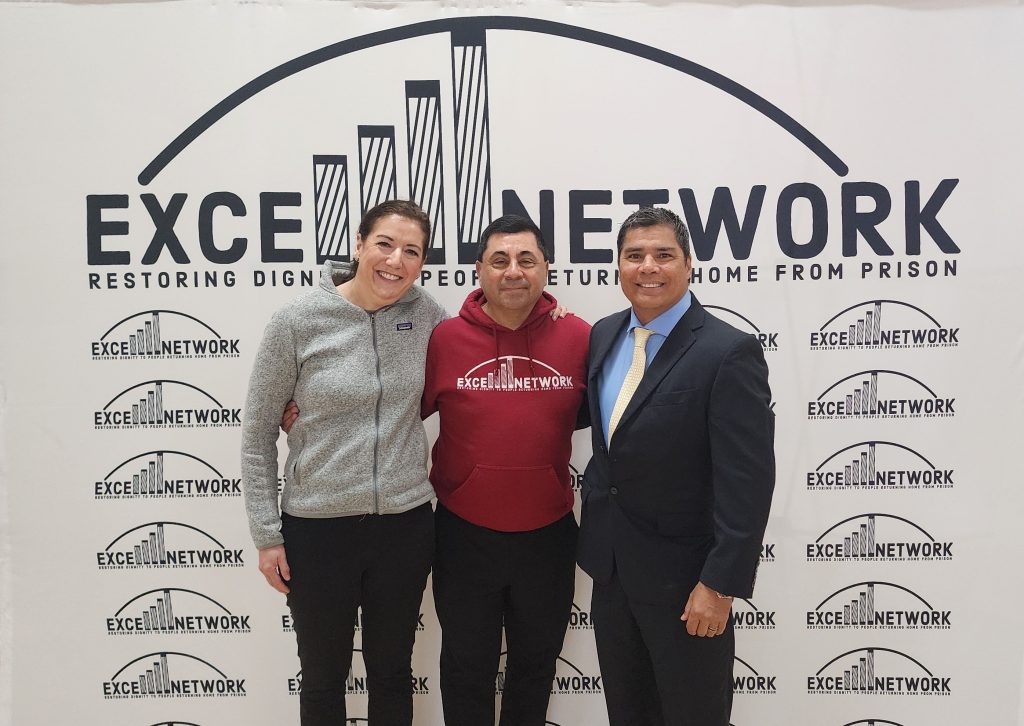 Three people standing in front of the Excell Network banner.