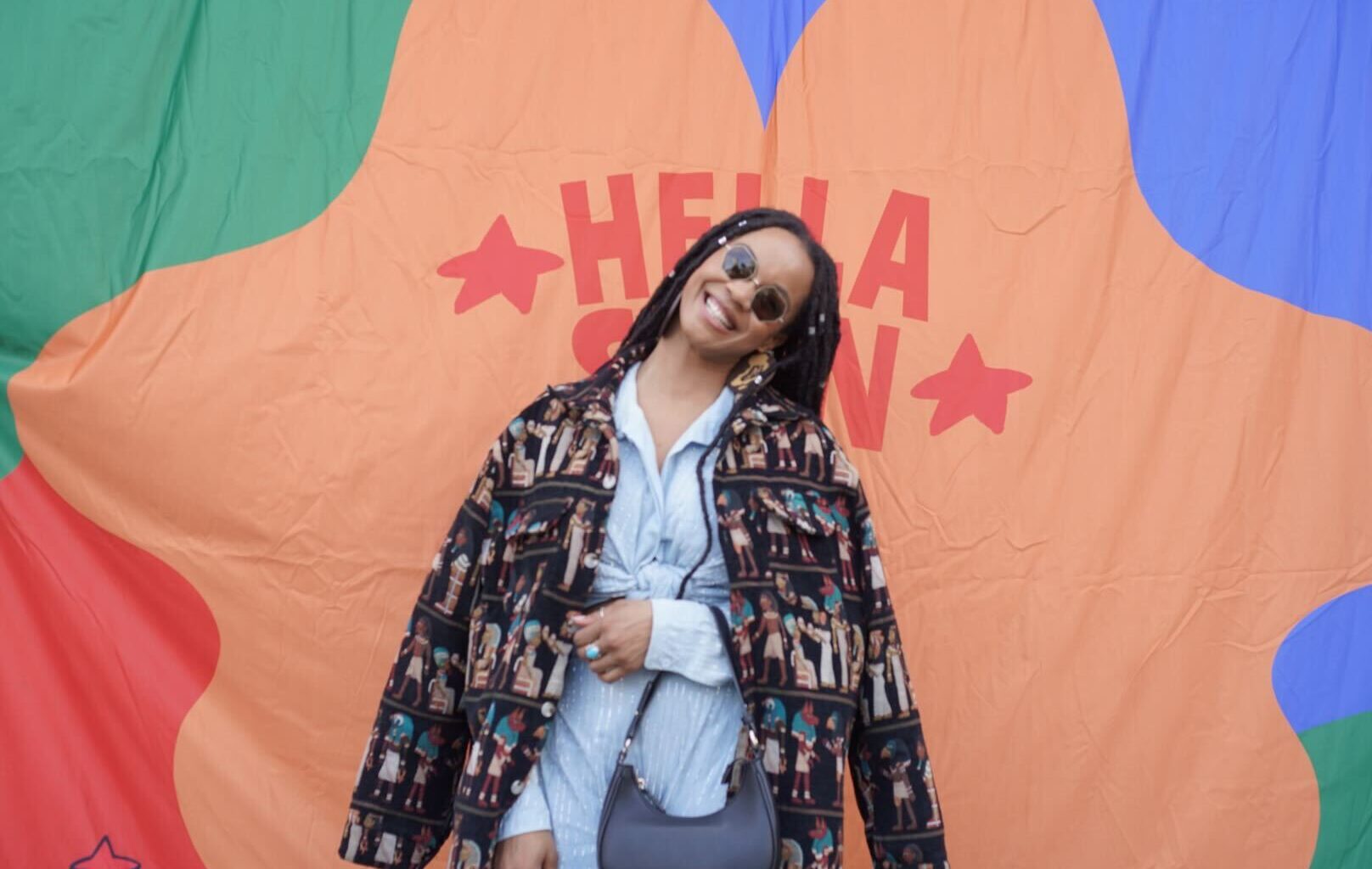 A Black woman with braids poses in front of a colorful background.