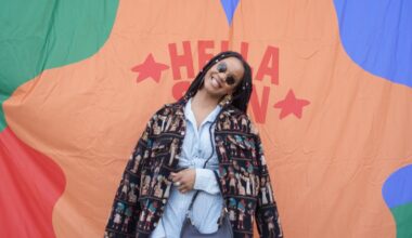 A Black woman with braids poses in front of a colorful background.