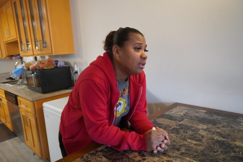 A woman in a red sweater leans on a table in a kitchen