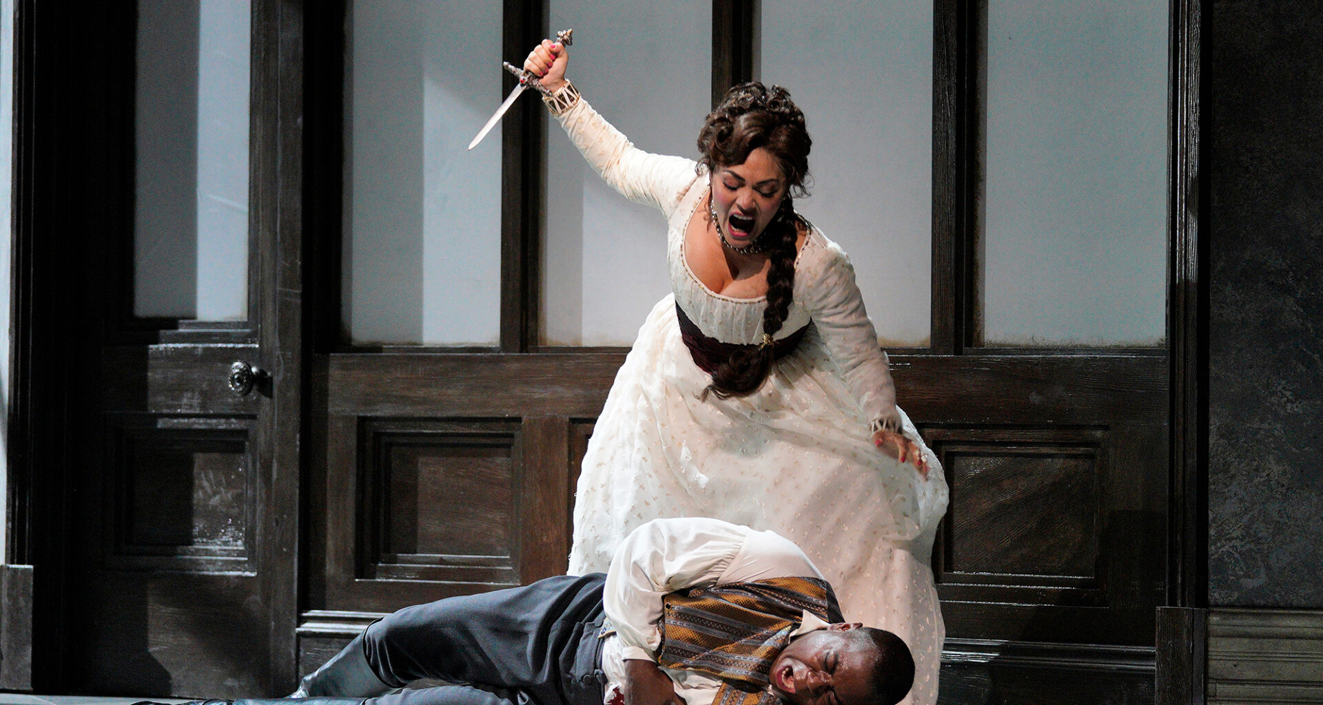 A woman in white hoists a dagger above a man laying on the ground