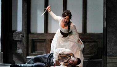 A woman in white hoists a dagger above a man laying on the ground
