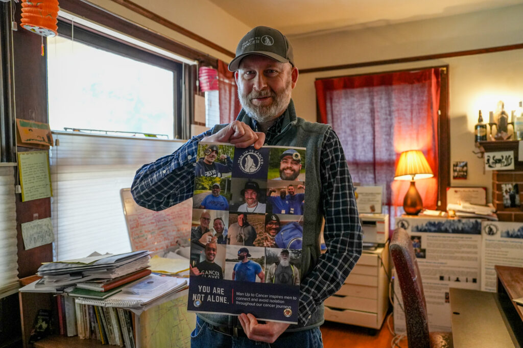 Brad Buchanan, NorCal chapter leader of Man Up to Cancer, holds a sign from the organization in his home. Photo by Denis Akbari.