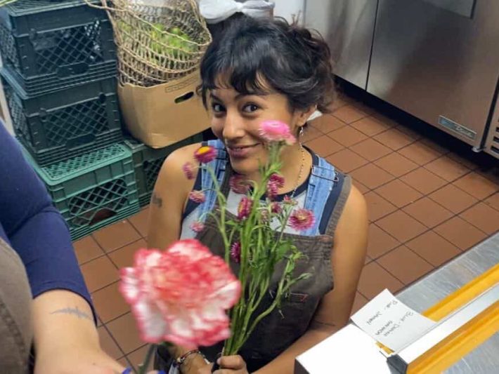 a woman in a professional kitchen smiles with a bouquet of flowers