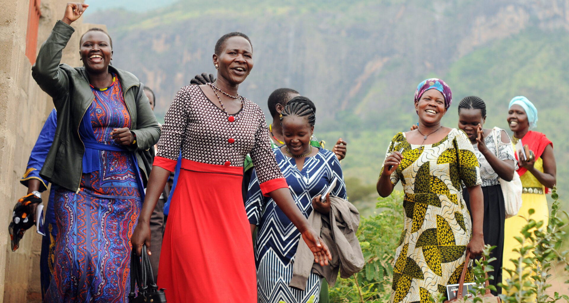 A half-dozen East African women smile and laugh as they walk by farm fields