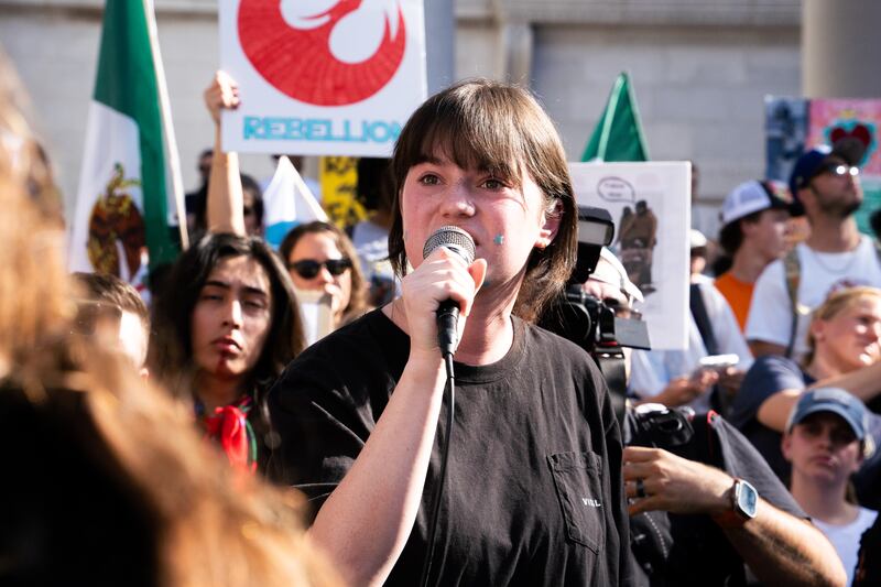A short-haired young woman holds a microphone in the center of the crowd.