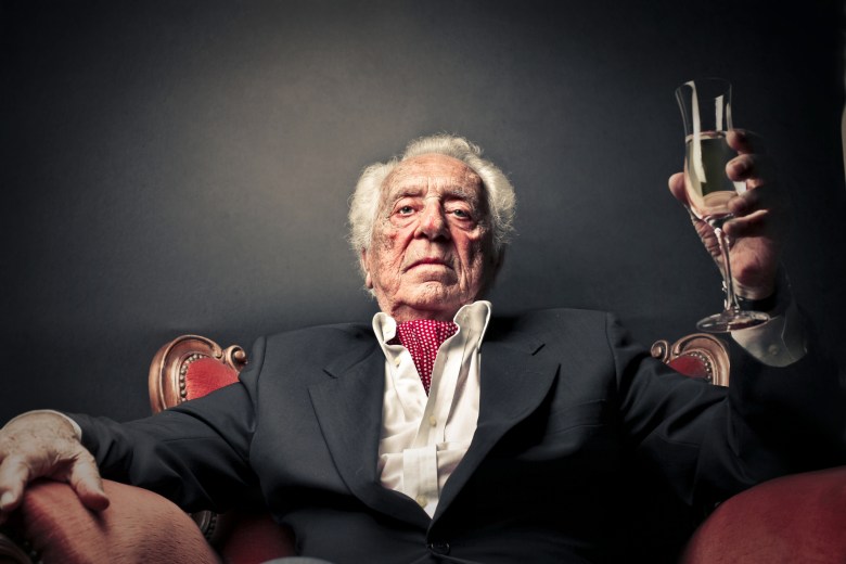 An old man in fancy clothes raises a glass of Champagne