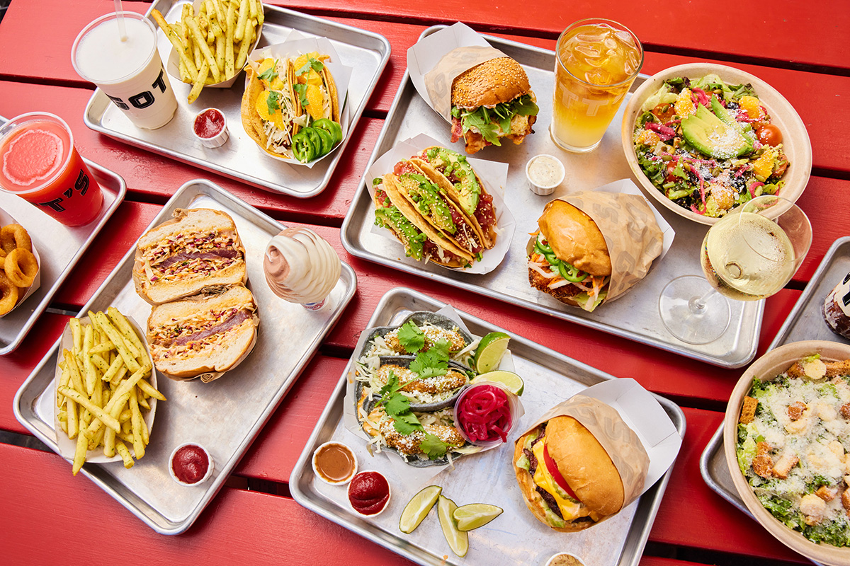 Overhead shot of a spread of dishes at Gott’s Roadside including burgers and tacos on a red table.