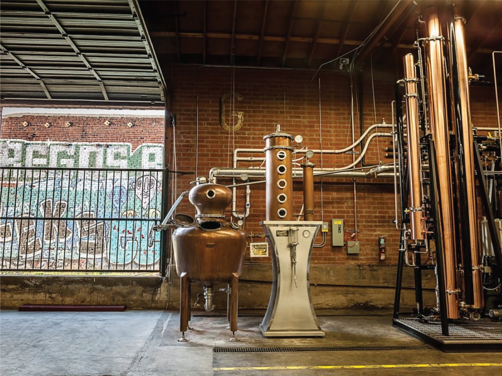 Interior of Greenbar Distillery in Los Angeles, showing distillation equipment and a view of graffiti outside.