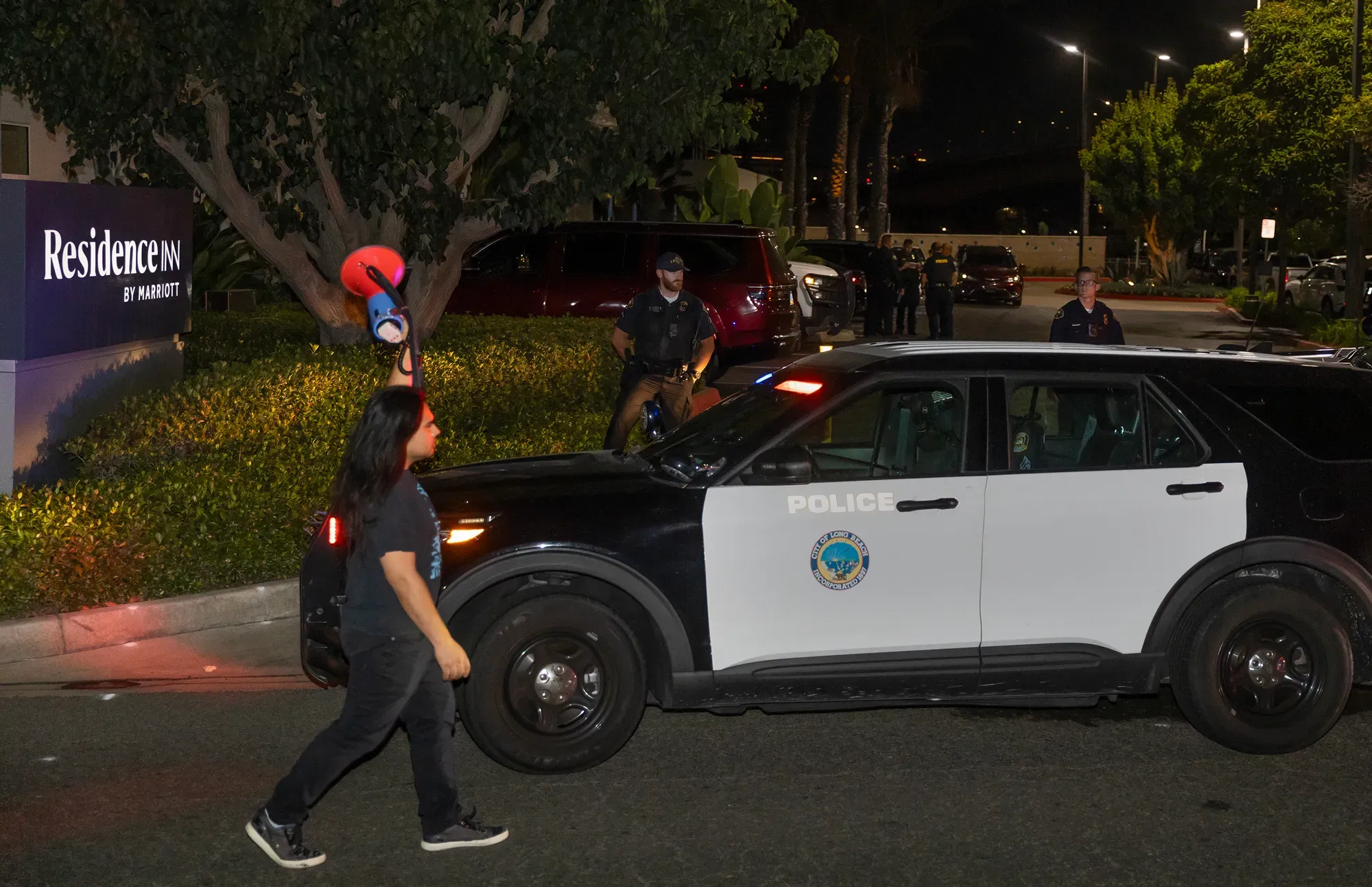 A person holding a bullhorn walks past a police car at night.