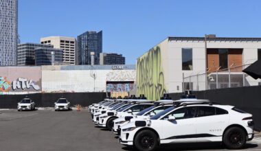 A group of Waymo cars parked in a parking lot.