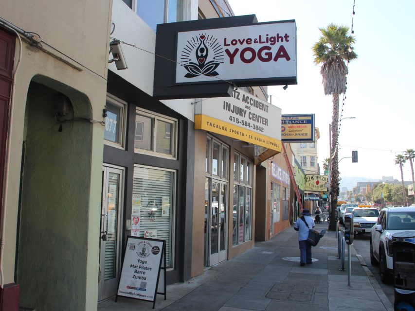 Street view of Excelsior storefronts, including "Love & Light Yoga" and "Kiz Accident Injury Center"; sidewalk sign lists yoga, mat pilates, barre, and zumba classes; a person stands nearby.