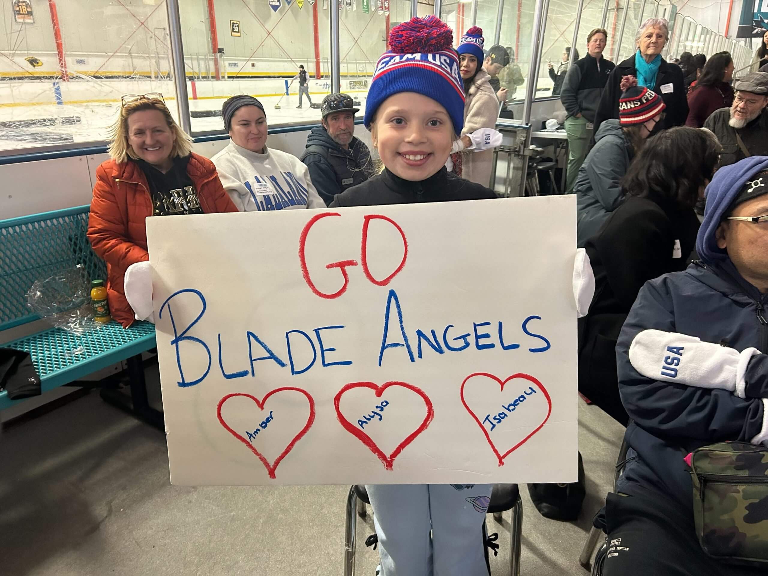 A young girl holds up a cardboard sign that reads "Go Blade Angles."