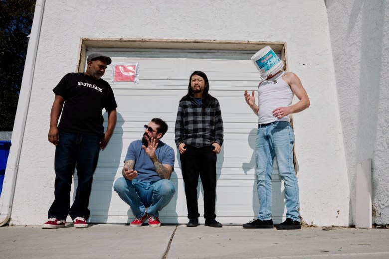 Members of The Sines stand In front of a white garage with a "red tag" on the door because it was condemned