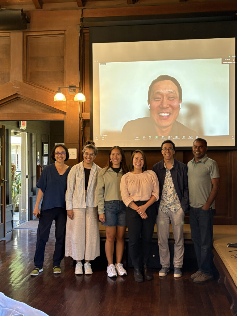 A group of academics stand in front of a projection of someone else, who is smiling on Zoom