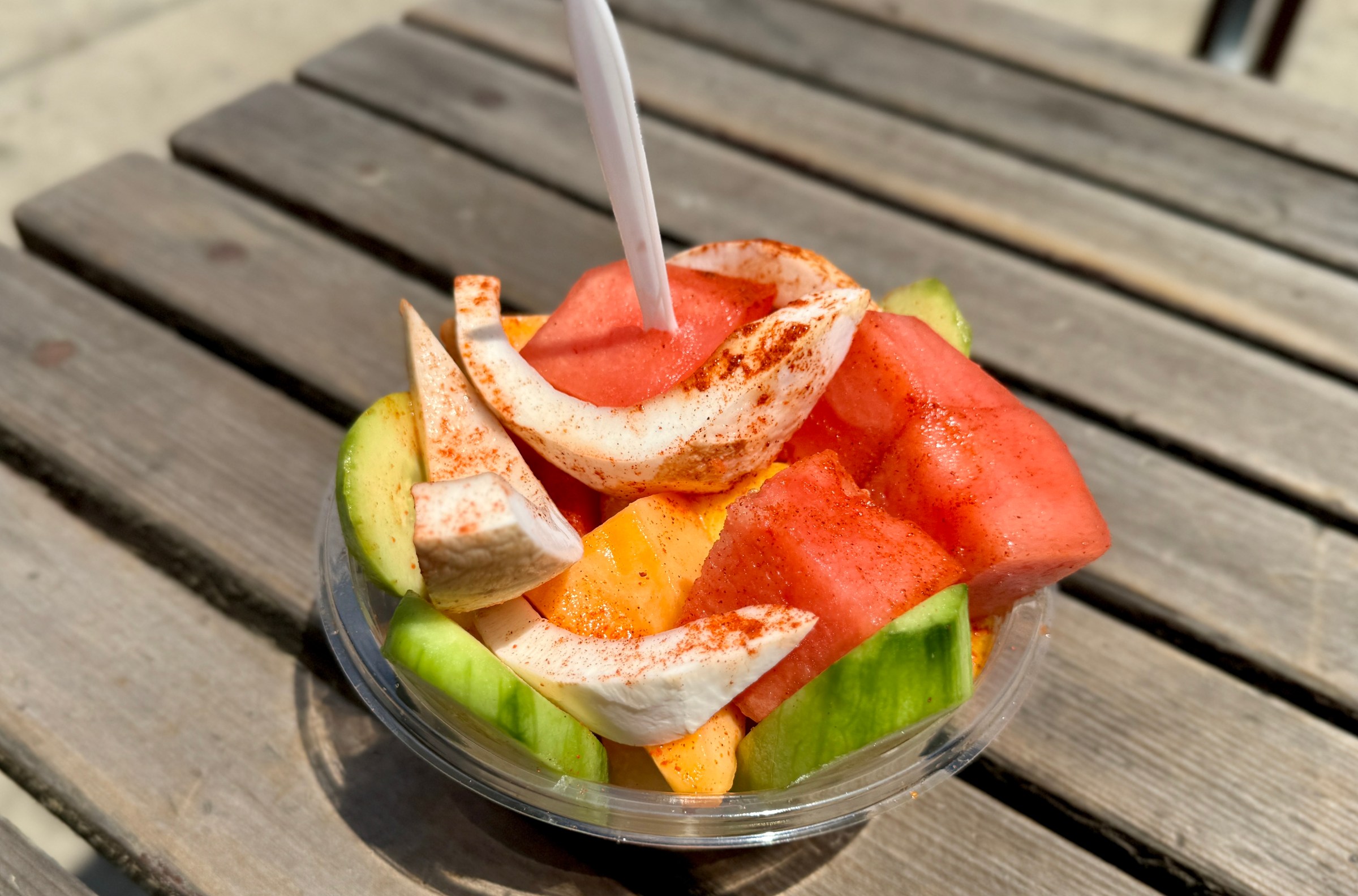 Sliced fruit from Rico Tejuino Los Reyes in a plastic bowl with a fork in the top 