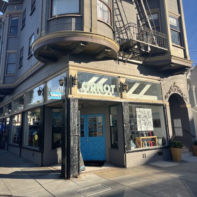 A street corner storefront with a sign reading "ORNOT," featuring blue double doors, large windows, and a decorative upper façade.