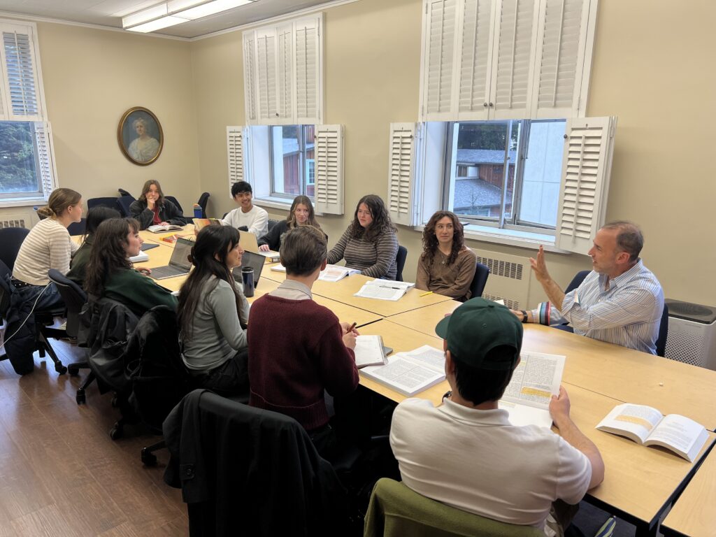 A group of students sit around a table, talking with a professor.