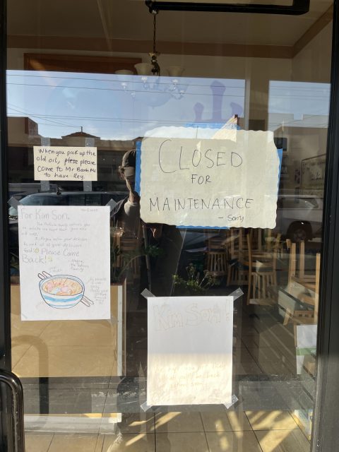 Glass door with handwritten signs, including one reading “Closed for maintenance sorry”; empty restaurant and wooden chairs visible inside.