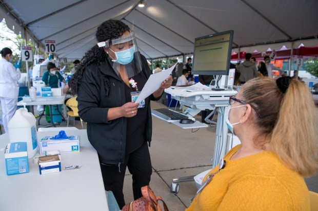 FILE -- LA County Department of Health Services Supervising Clinic Nurse Jamie Robledo asks health questions to Loly Lemus, Nursing Attendant, at a COVID-19 vaccination clinic at LAC+USC Medical Center, Dec. 18, 2020. (Photo County of Los Angeles/Michael Owen Baker)