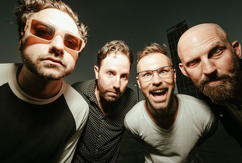 A heavily shadowed photo of four male band members making silly faces