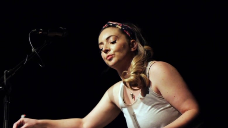 A woman in a tank top making electronic music against a black background