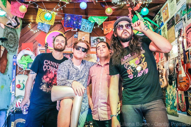 Four male band members pose amid a crazy party atmosphere