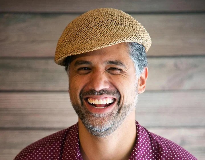 Headshot of a smiling man with a beard wearing a woven cap