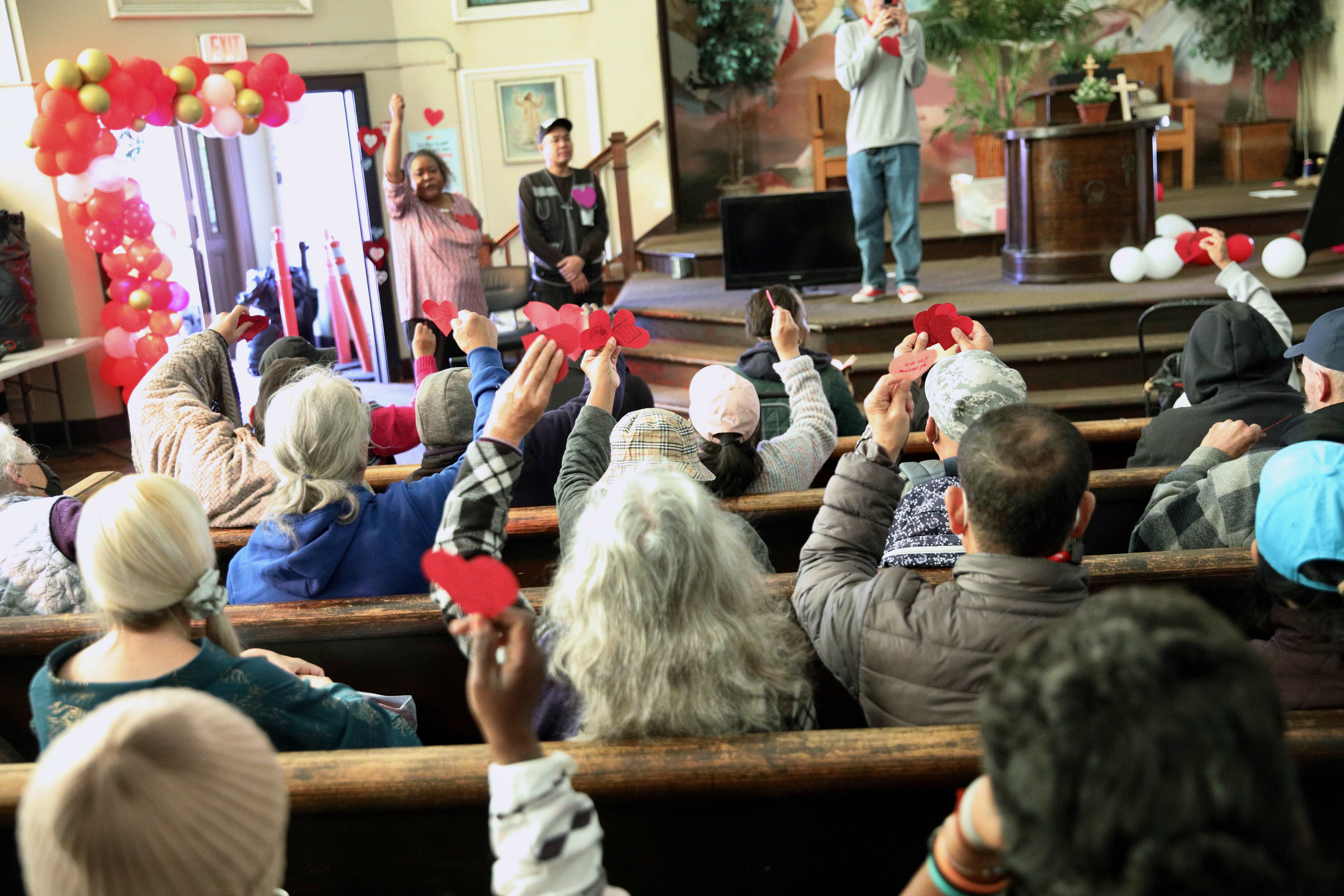 Community members raise paper hearts with loving messages distributed by...
