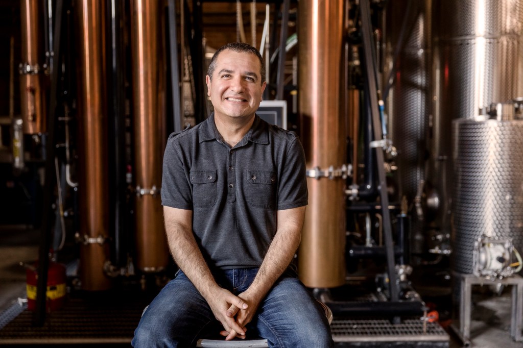 Melkon Khosrovian, owner of Greenbar Distillery, sitting in front of distillery equipment.