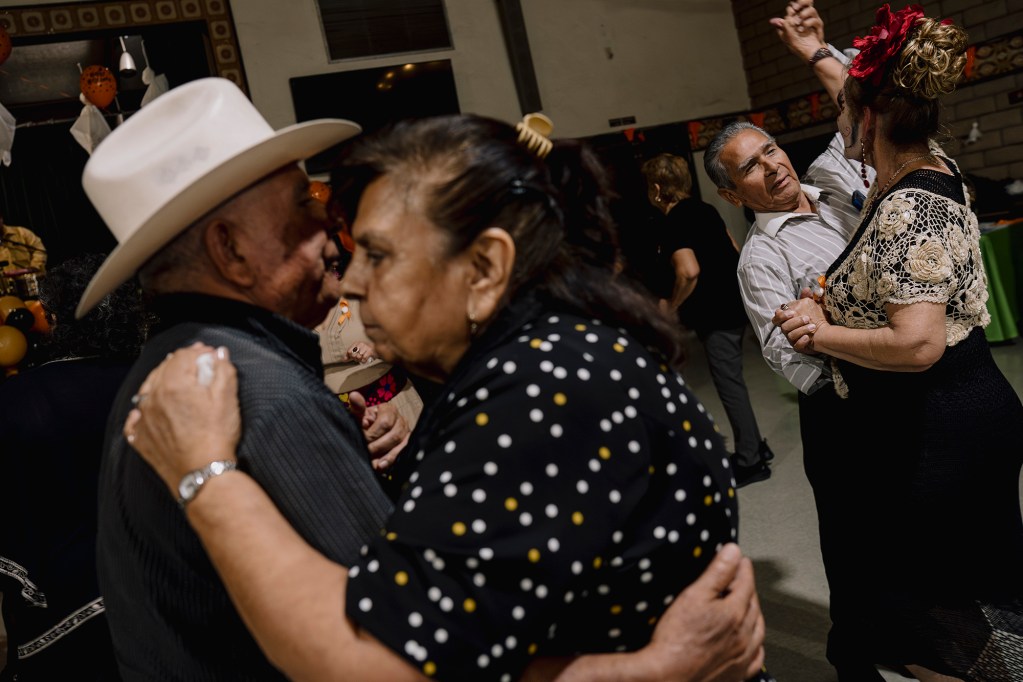 Two older couples dance closely together at an indoor celebration, one pair in the foreground embracing while another turns mid-step in the background.