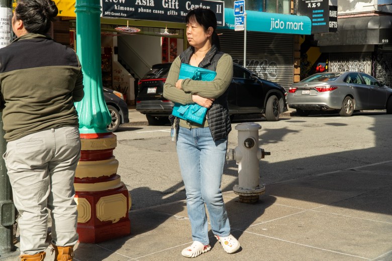 A woman clutches a notebook standing on a street corner in Chinatown