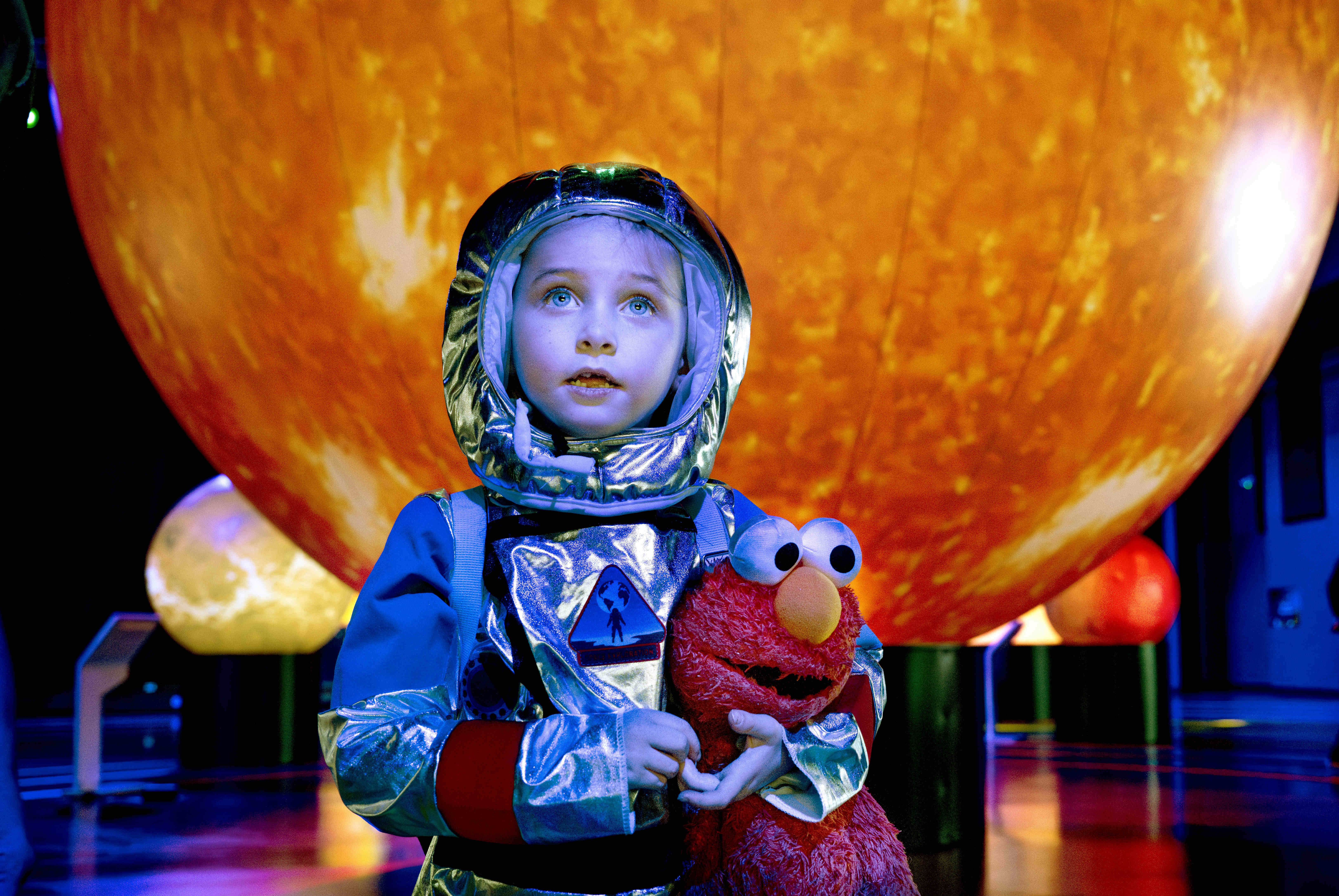 Dressed like an astronaut and holding her stuffed Elmo doll,...