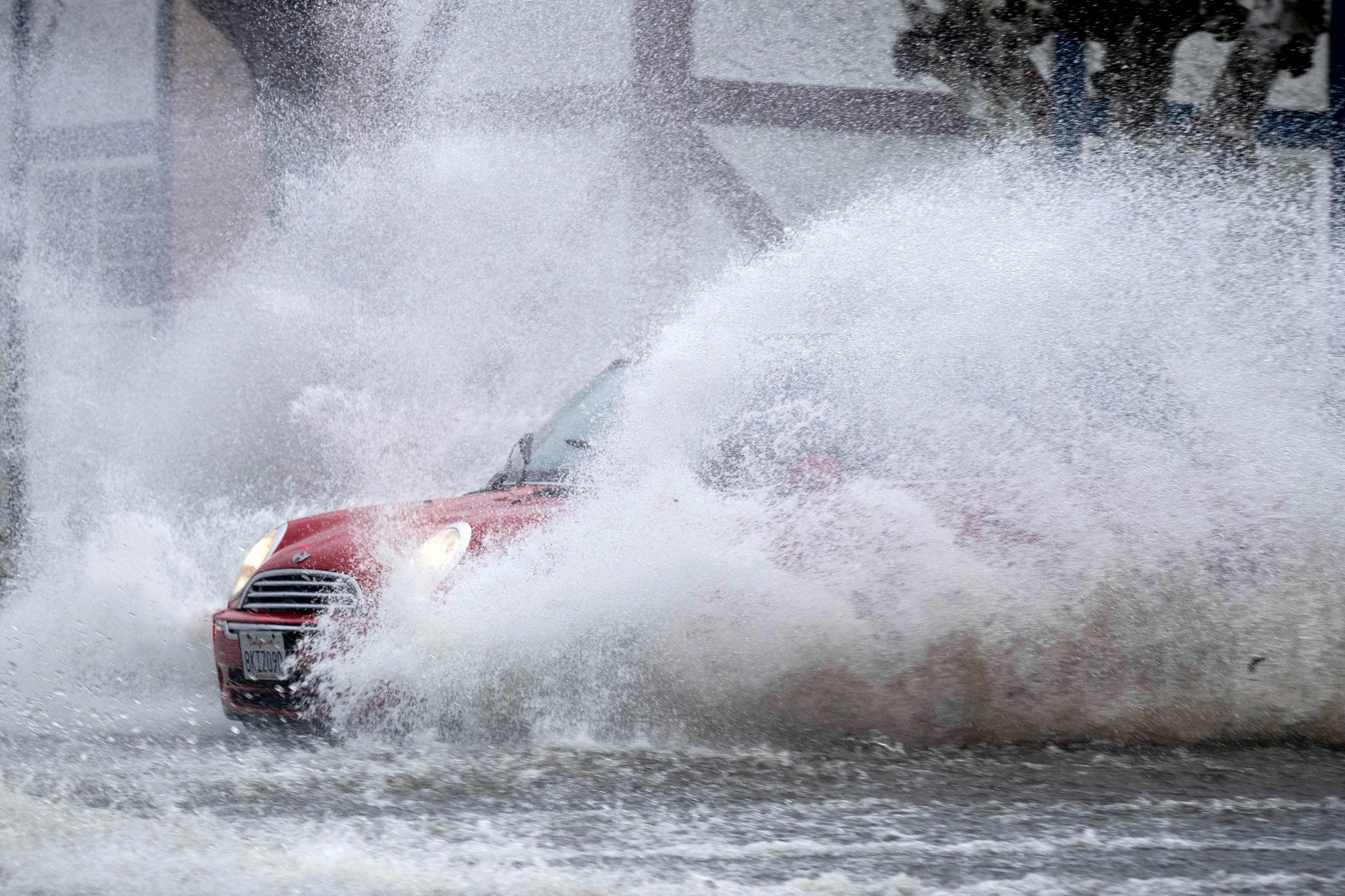 A Mini Cooper drives along Vanowen Street while crossing flooded...