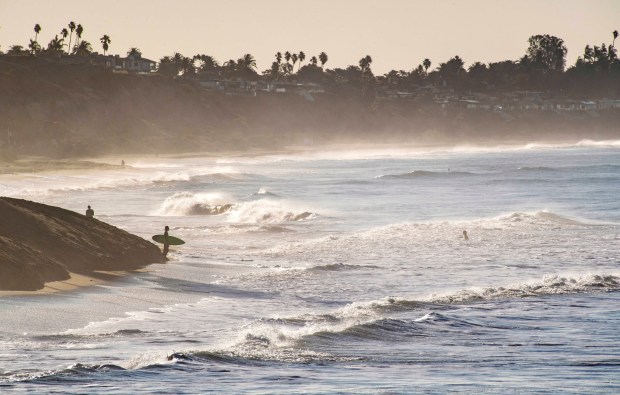 A surfer stands at the edge of a sand berm and checks out the waves before entering the water just south of the San Clemente Pier as a king tide moves on shore in 2020. (Photo by Mark Rightmire, Orange County Register/SCNG)