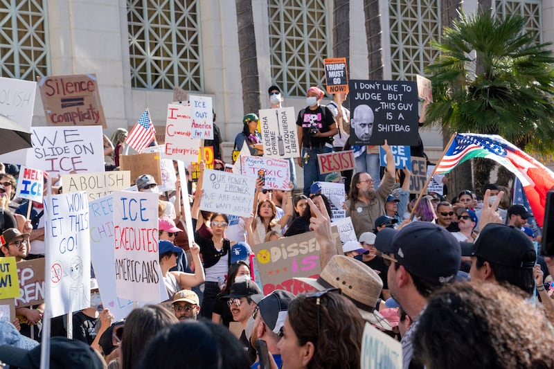 Protesters hold signs that read: "ICE executes Americans," " Silence = complicity," Our power to empower, we are angry we want justice," "Resist," and "I don't like to judge but this guy is a shitbag (arrow pointing to Stephen Miller)."