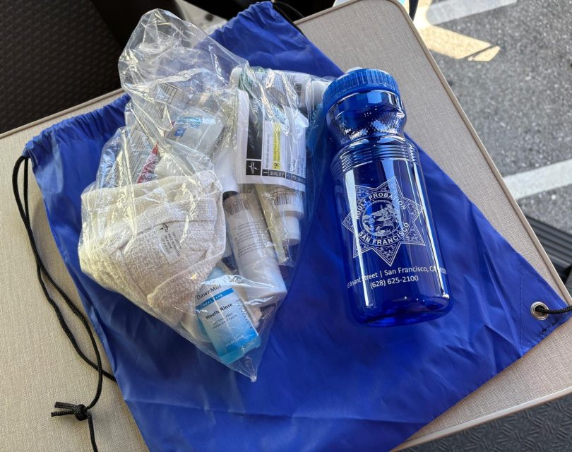 A blue drawstring bag, a clear plastic bag containing medical supplies, and a blue water bottle are placed on a table.