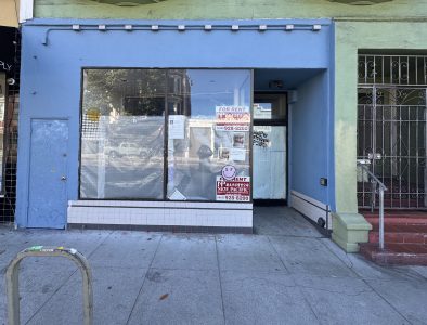 A vacant storefront with a blue facade displaying multiple "For Rent" signs in the window, located on a city sidewalk.