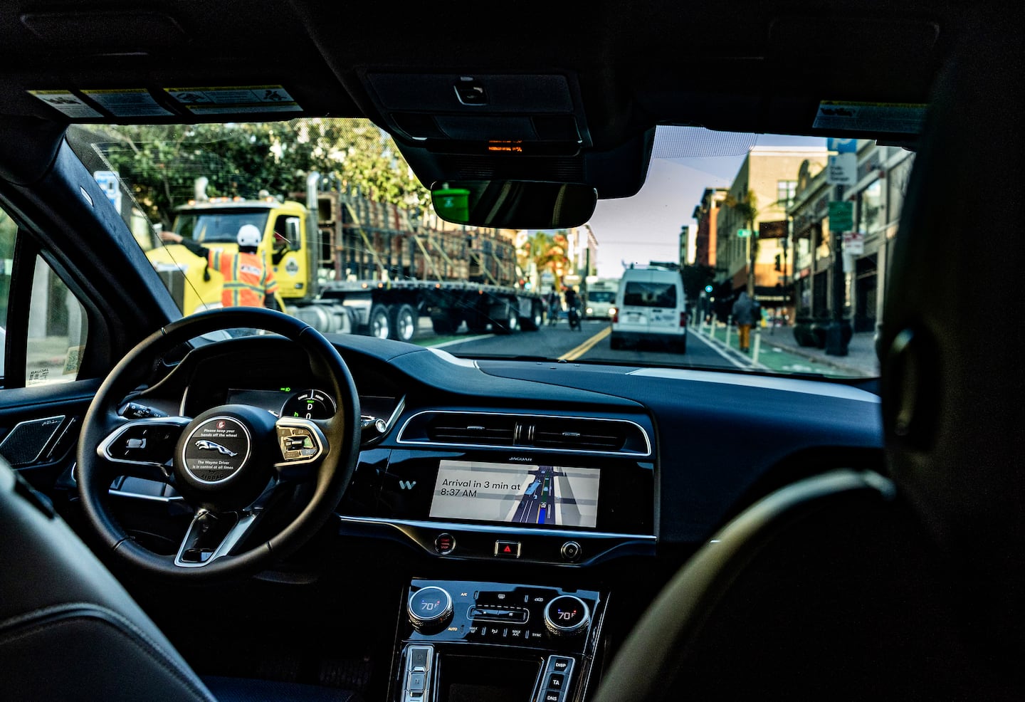 A self-driving Waymo heading up a hill waits as a truck makes a right turn, even though there is space straight ahead.  