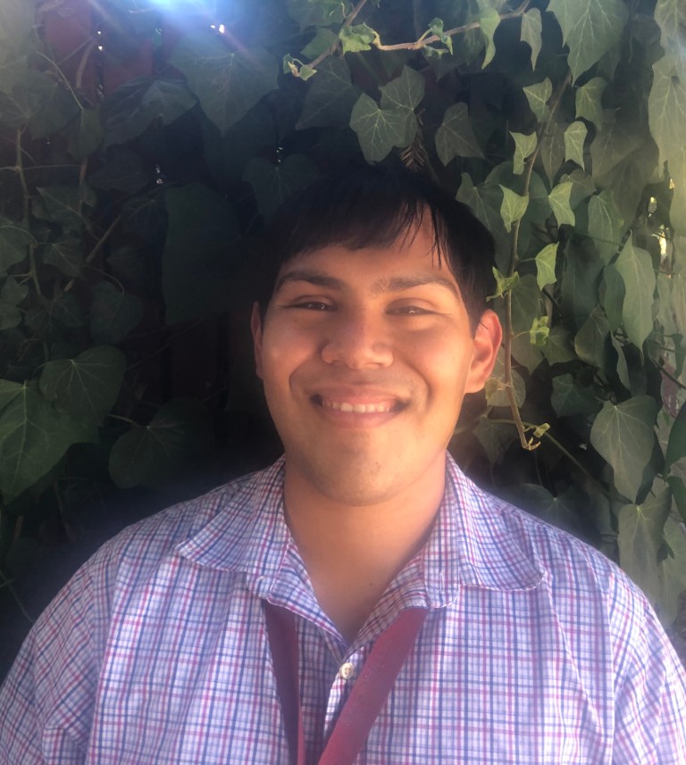 Headshot of a smiling assistant principal against a leafy green background.