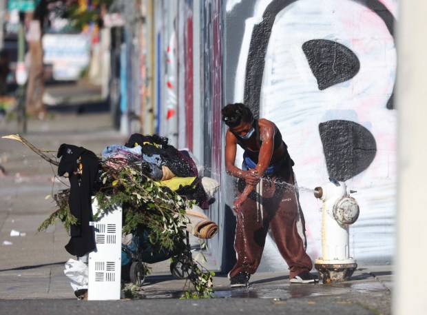A woman uses a fire hydrant to bathe along 18th Avenue on Tuesday, Jan. 13, 2026, in Oakland, Calif. (Aric Crabb/Bay Area News Group)