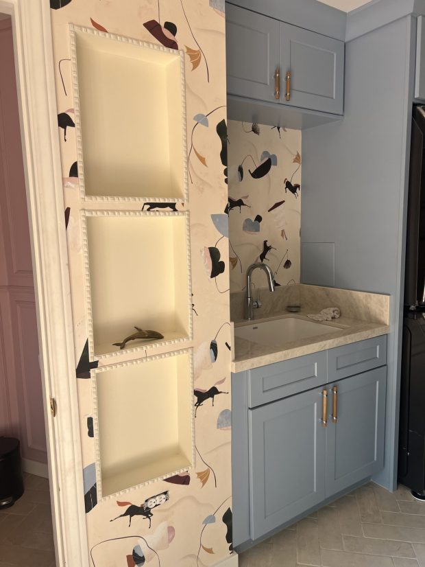 A breezy, playful wallpaper set the vibe for this laundry room transformation by Carmen Coutts. A deep sink with cupboards was installed next to niche cutouts for decorative items. (Daughters of Design)