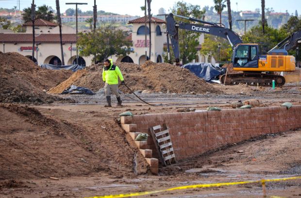 2/18/2026_San Marcos, CA_A construction worker drags a water hose along a recently built retaining wall on the former site of Old California Restaurant Row. The site is now under construction for residential and commercial buildings. In the distance along the west end of the property is the food court area of nearby Edwards Cinemas theaters. (Charlie Neuman / For The San Diego Union-Tribune)