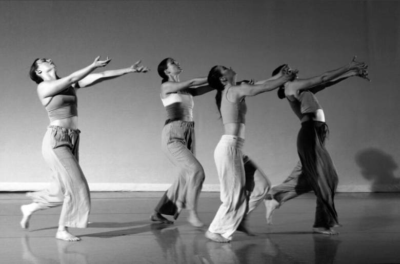 Four people in tank tops and loose pants dance in a black and white photo
