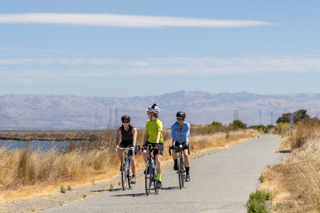 Three people riding bikes on a path at a park in Mountain View, California