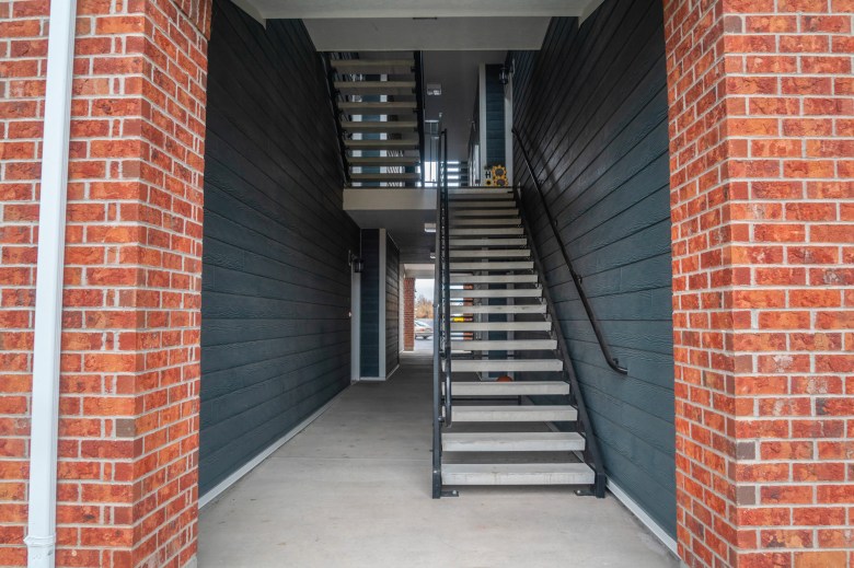 An outdoor opening of a brick building that leads to a flight of stairs in between apartment units.