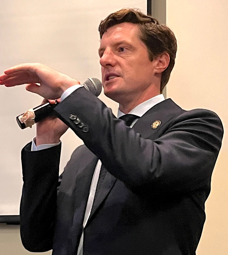 A man in a suit speaks into a microphone.