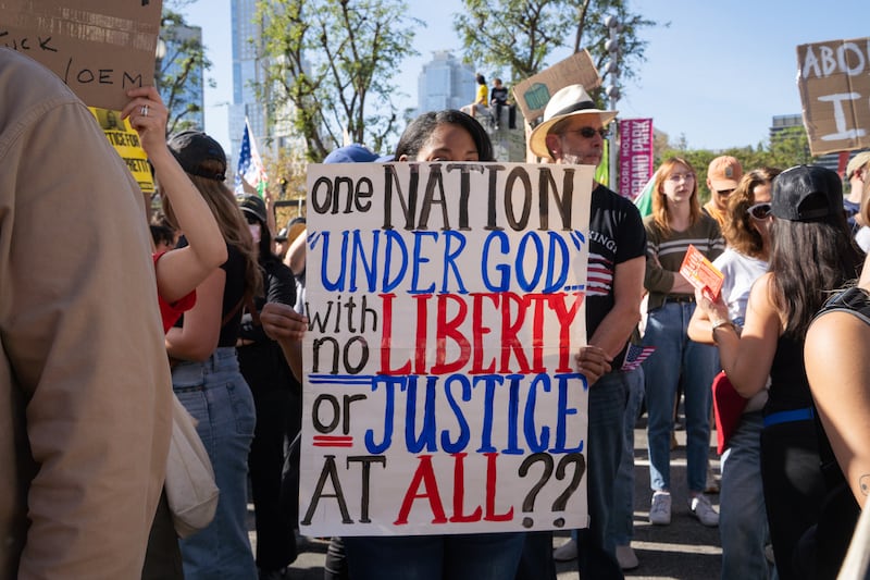 A protester holds a sign reading "one nation 'under god' with no liberty or justice at all??"