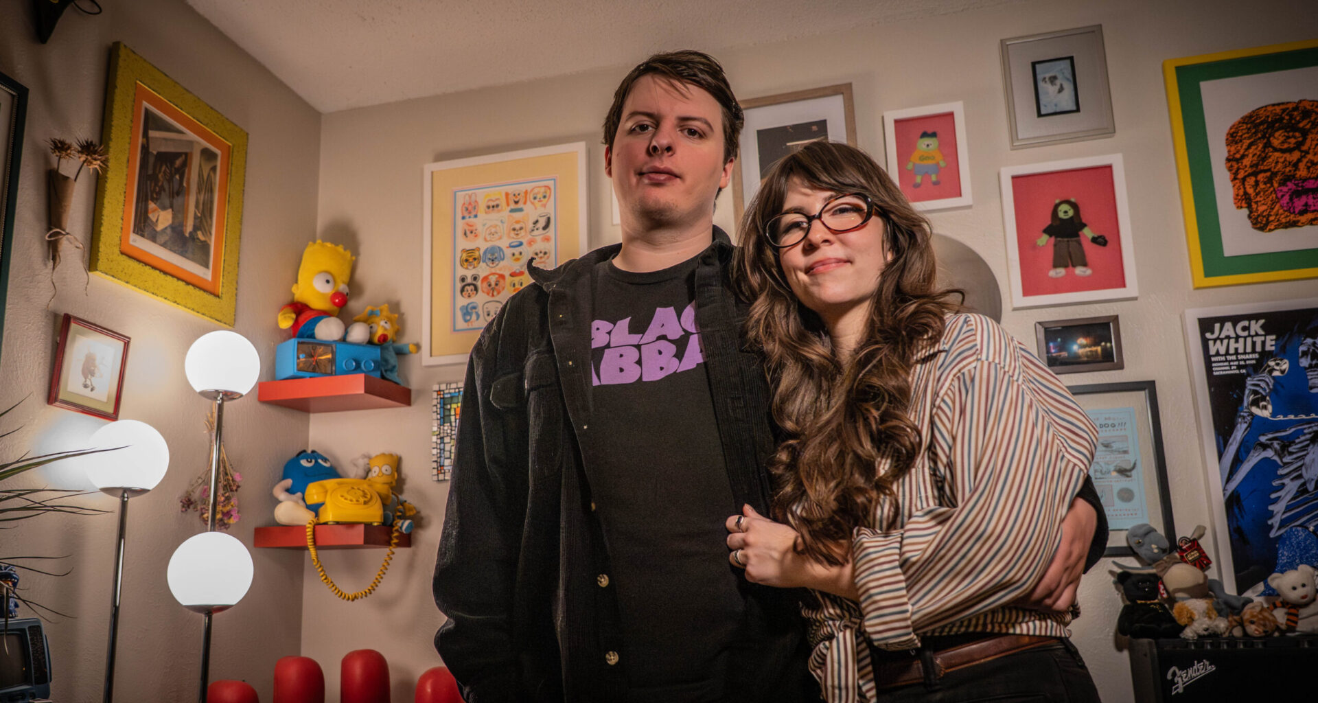 Avery McPherson and Alisa Turner pose in front of their wall of art and memorabilia in their home.