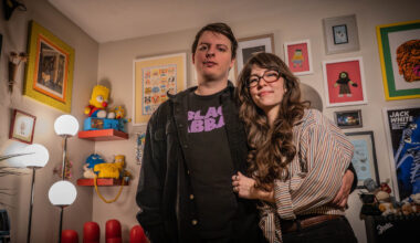 Avery McPherson and Alisa Turner pose in front of their wall of art and memorabilia in their home.